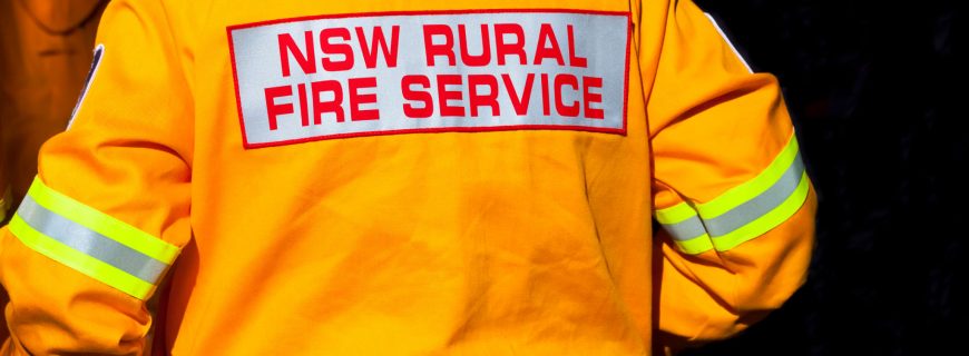 Closeup rear view of firefighter with yellow protective  jacket with logo of 'NSW RURAL FIRE SERVICE' Australia, full frame horizontal composition with copy space