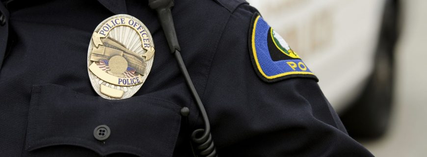 a close up of an officers uniform and badge with a patrol car in the background.